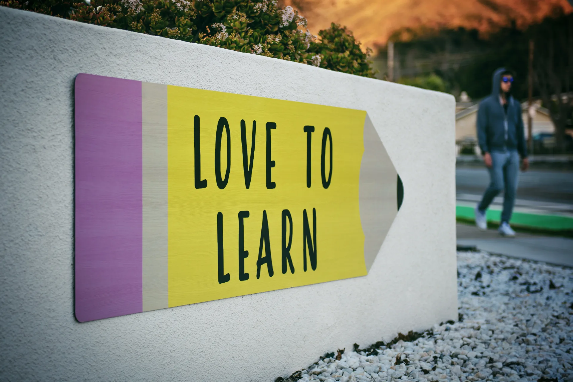 Ein Schild mit der Aufschrift "LOVE TO LEARN" an einer Mauer mit einem vorbeigehenden Fußgänger im Hintergrund.