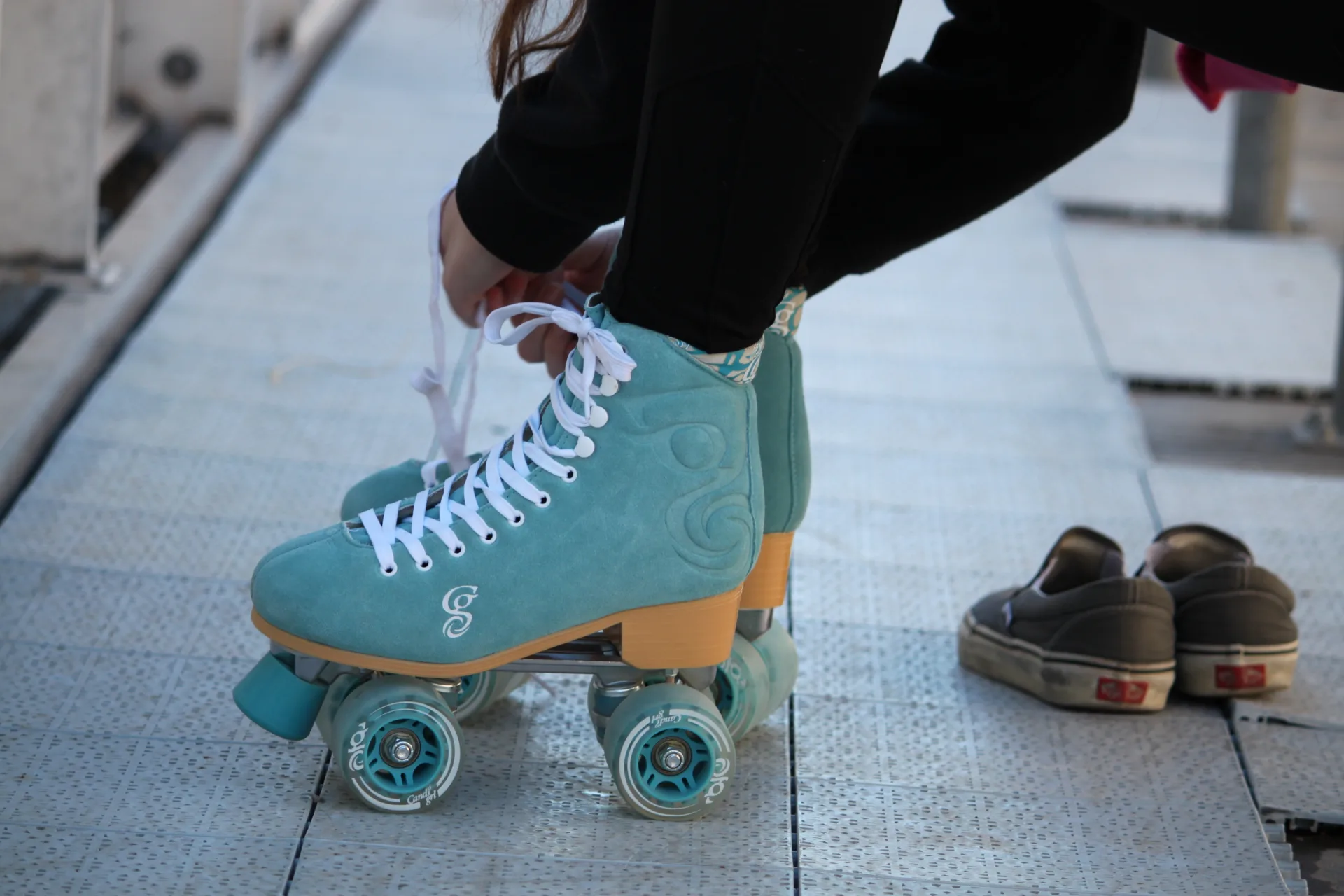 Bewegung gegen Schulstress – ein junges Mädchen bindet die Schnürsenkel an türkisfarbenen Rollschuhen mit weißen Schnürsenkeln; abgestellte Sneaker sind im Hintergrund sichtbar.