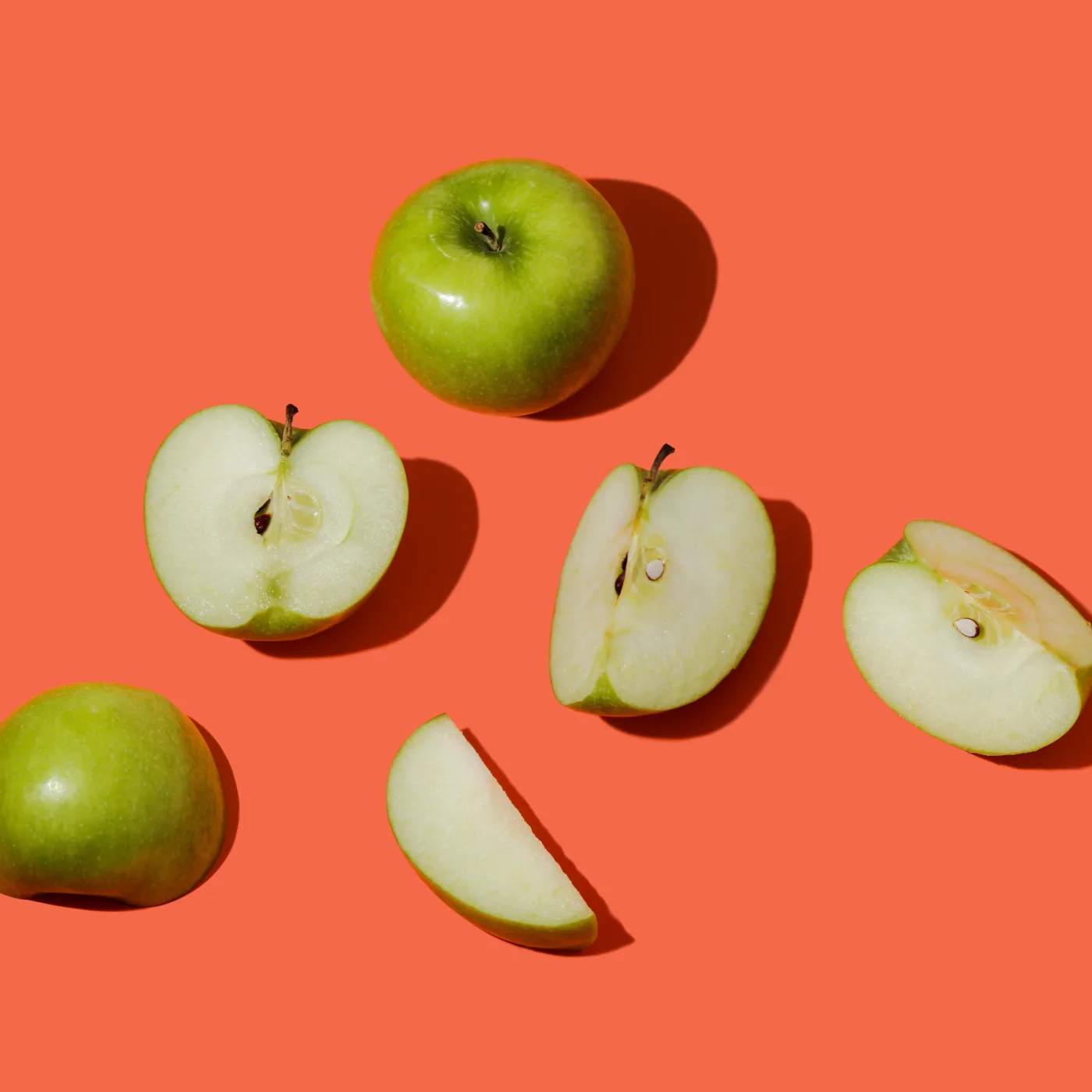 Ernährung gegen Schulstress – Grüne Äpfel und Apfelscheiben auf einem leuchtend orangefarbenen Hintergrund.