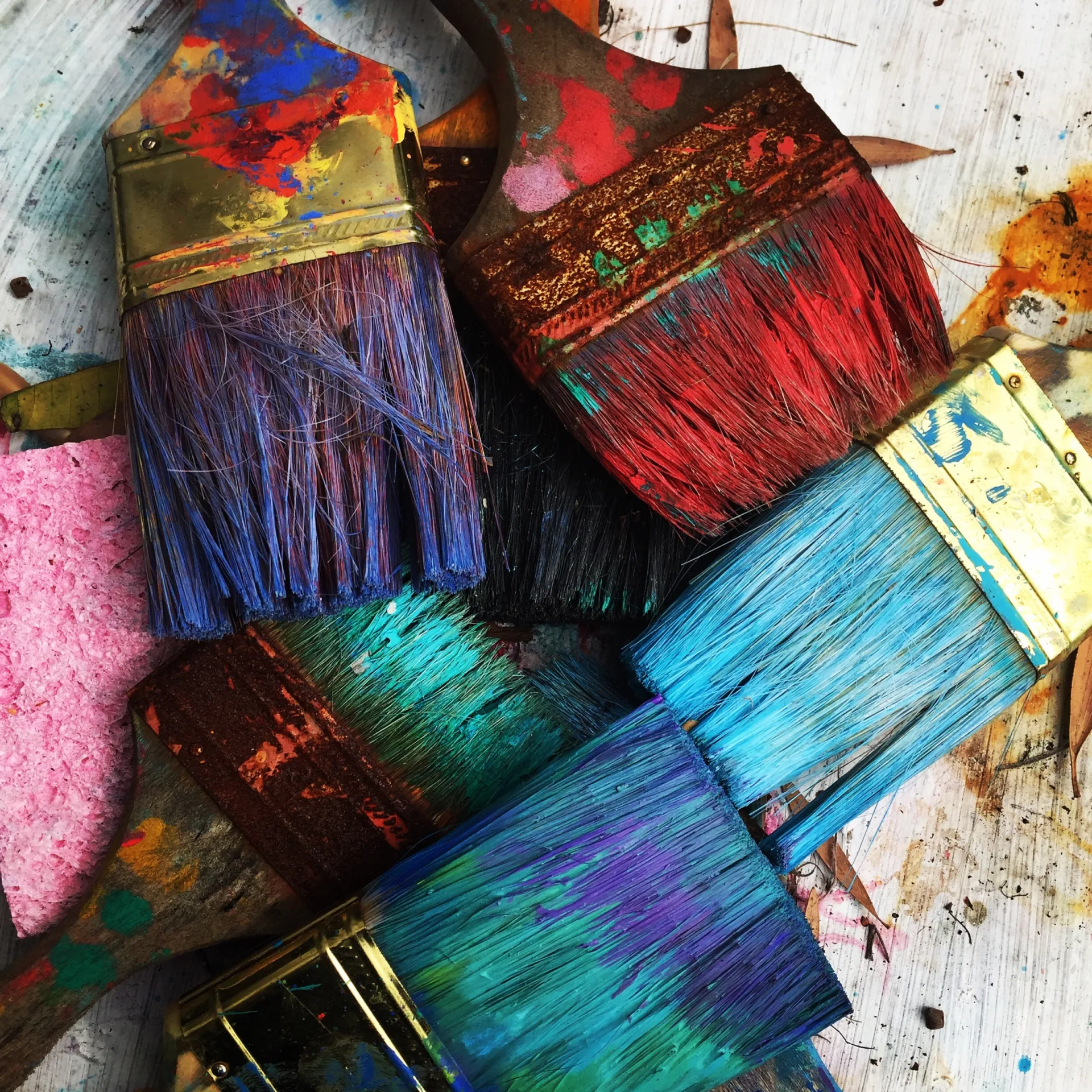 Verschiedenfarbige, mit Farbe verschmierte Pinsel liegen kreuz und quer auf einem mit Farbspritzern bedeckten Untergrund - Kreative Pause bei Schulstress.