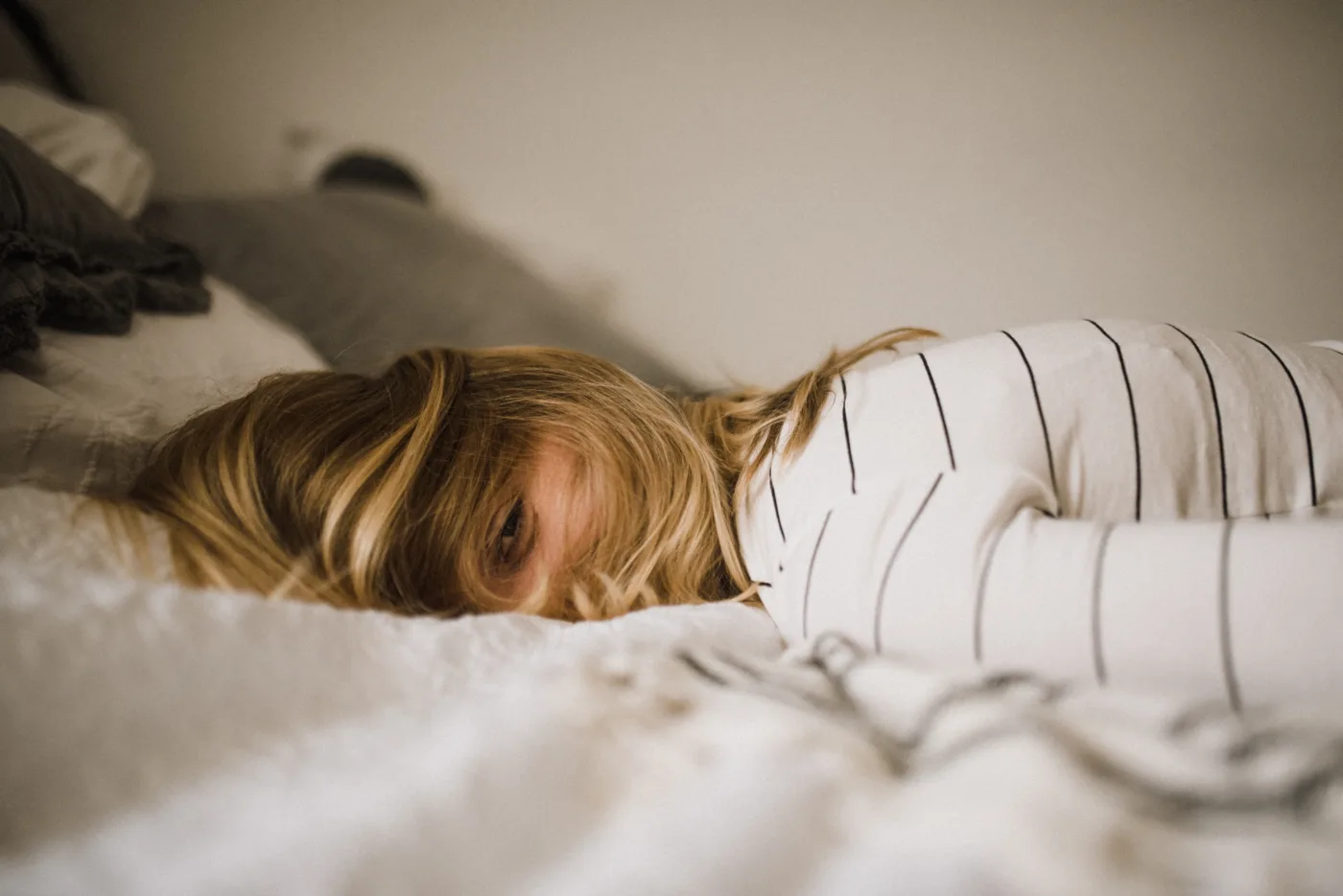 Schlaf gegen Schulstress – Eine Person liegt erschöpft im Bett, nur das Gesicht ist sichtbar, umgeben von Bettwäsche.