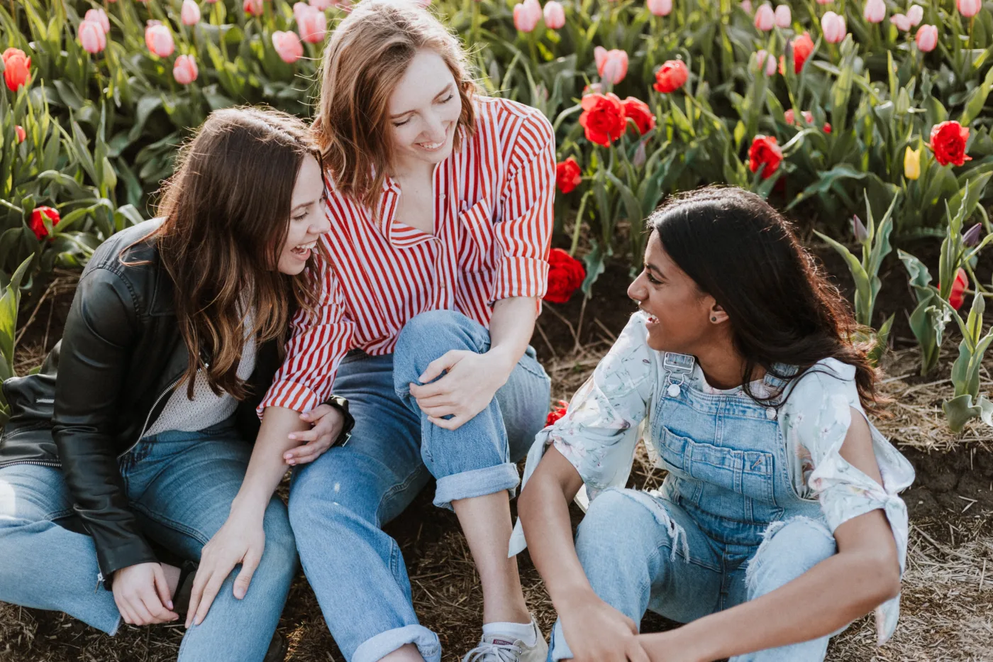 Ausgleich bei Schulstress – drei Mädchen sitzen an einem Tulpenfeld und lachen miteinander