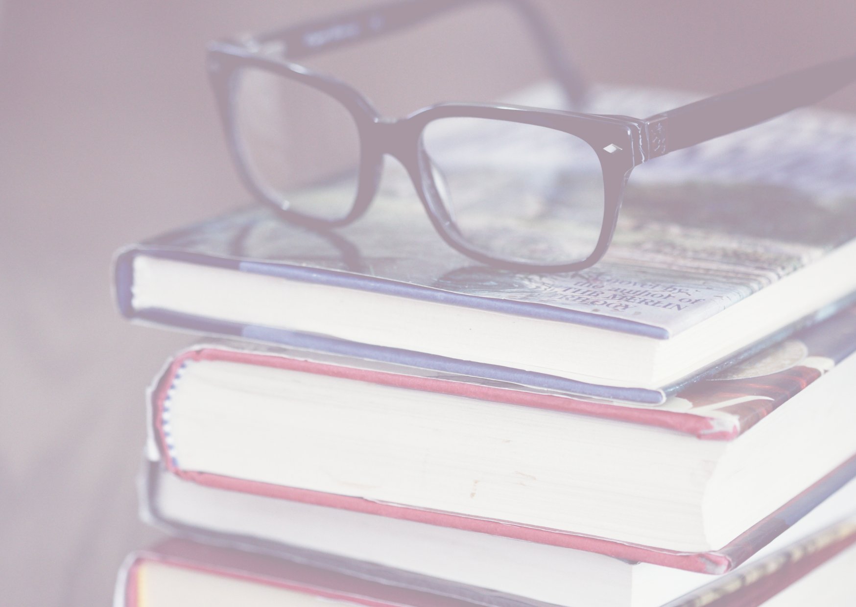 Ein Stapel von gebrauchten Büchern mit einem Paar schwarzer Brillen oben auf. Die Bücher scheinen gut gelesen zu sein, was auf einen eifrigen Leser oder einen engagierten Studenten hindeutet. Die sanften Farben und die weiche Fokussierung verleihen dem Bild eine ruhige und studiöse Atmosphäre.