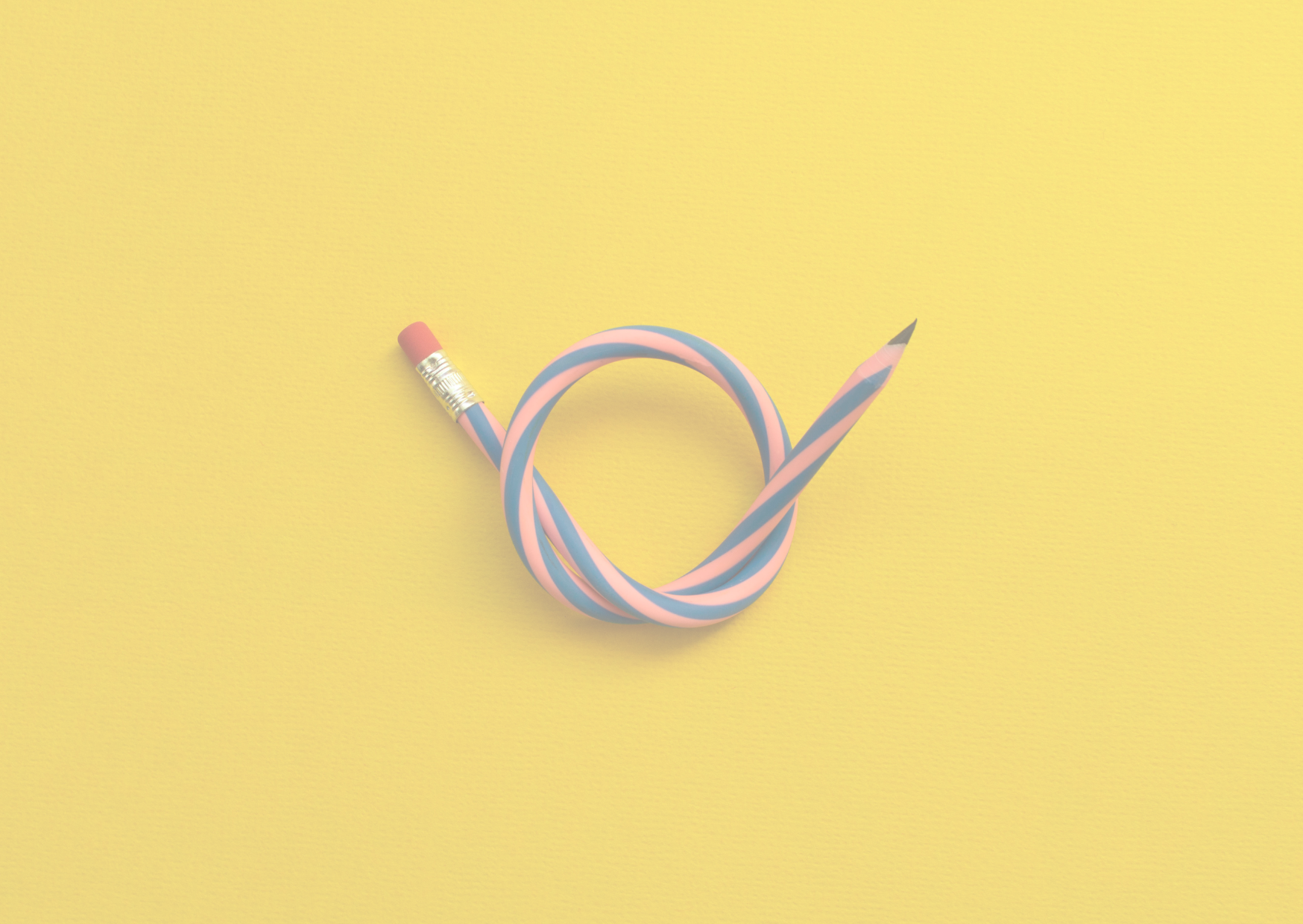 Ein einfacher Bleistift mit Radiergummiende liegt auf einem einfarbigen gelben Hintergrund und ist so gebogen, dass er eine Schleifenform bildet, was Kreativität und Flexibilität im Denken symbolisiert.