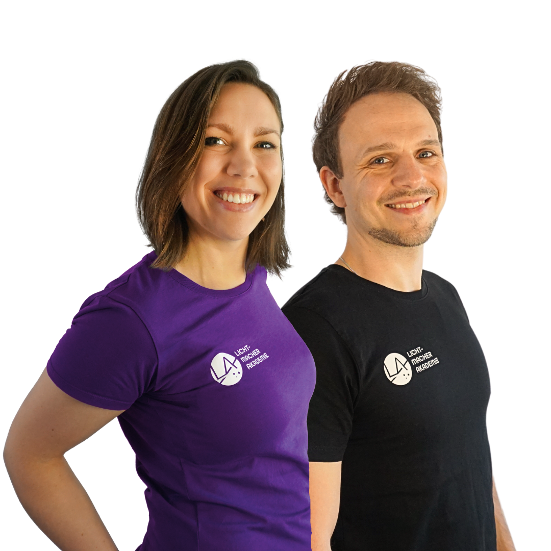 Zwei Lächelnde Teammitglieder der Lichtmacher Akademie in Firmenkleidung, stehend vor einem weißen Hintergrund.